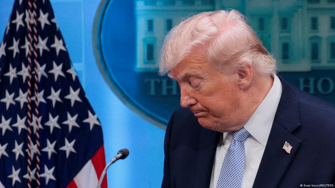 Donald Trump camina cabizbajo frente a una bandera de Estados Unidos.