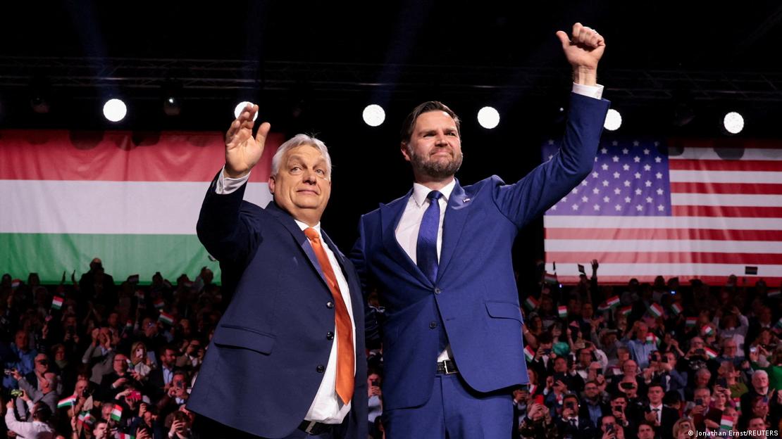 Macaristan Başbakanı Viktor Orban ve ABD Başkan Yardımcısı JD Vance, iki ülke bayrakları önünde bir elleriyle birbirine sarılmış, diğer elleriyle kendilerini izleyen kalabalığı selamlıyor
