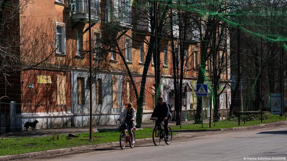 Dvoje biciklista na ulici iznad koje je razapeta mreža protiv dronova, Slavjansk u martu 2026.