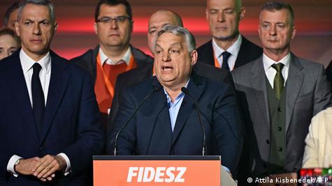 Унгарскиот премиер Виктор Орбан се обраќа од говорница на која го пишува името на неговата партија Фидес. Водечките членови на партијата стоејат околу него.