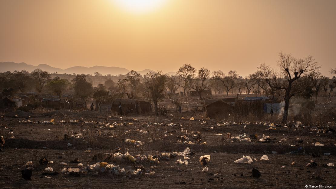 Área de vegetação escassa, com barracos e muitas sacolas plásticas espalhadas