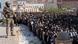 An armed guard stands above a group of Shiites praying An armed guard stands above a group of Shiites praying