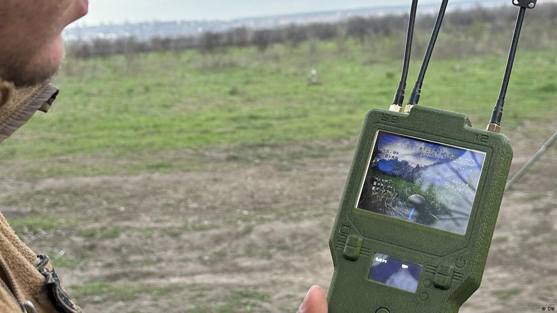 La foto muestra la barbilla de un soldado en un campo, sosteniendo una pantalla en la mano y observando la interceptación de un dron.