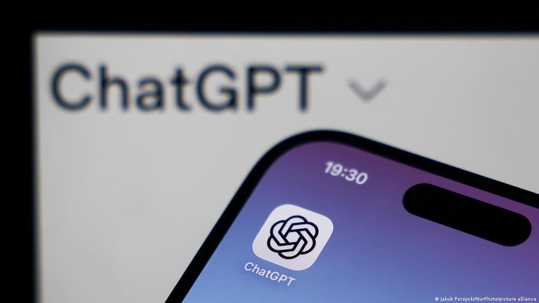 Bir akıllı telefon ekranındaki ChatGPT uygulama simgesi ile arka planda bir dizüstü bilgisayar ekranında görünen ChatGPT yazısı