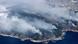 Aerial photo showing smoke rising above mountainous area at a coast Aerial photo showing smoke rising above mountainous area at a coast