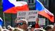 A person in a crowd holds up a placard. In the background are two large Czech flags, Brno, Czechia, April 28, 2026 A person in a crowd holds up a placard. In the background are two large Czech flags, Brno, Czechia, April 28, 2026