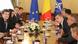 Mai mulţi oficiali stau de vorbă la o masă lungă, pe fundal se văd steagurile României, al UE şi al NATO Mai mulţi oficiali stau de vorbă la o masă lungă, pe fundal se văd steagurile României, al UE şi al NATO