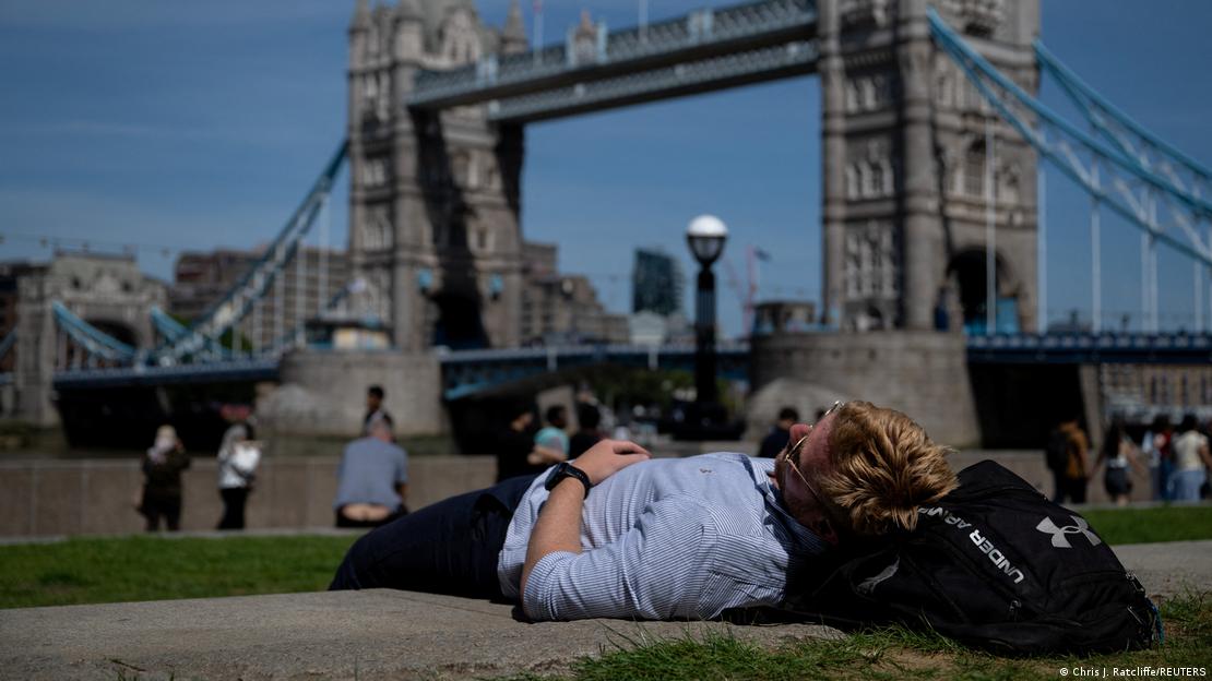 Un hombre recostado cerca del Tower Bridge en Londres durante la ola de calor.