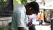 A young man uses an electric fan during a heat wave in London, seated near a black iron fence along a sidewalk A young man uses an electric fan during a heat wave in London, seated near a black iron fence along a sidewalk