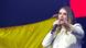 Paloma Valencia fala ao microfone em frente a uma bandeira da Colômbia