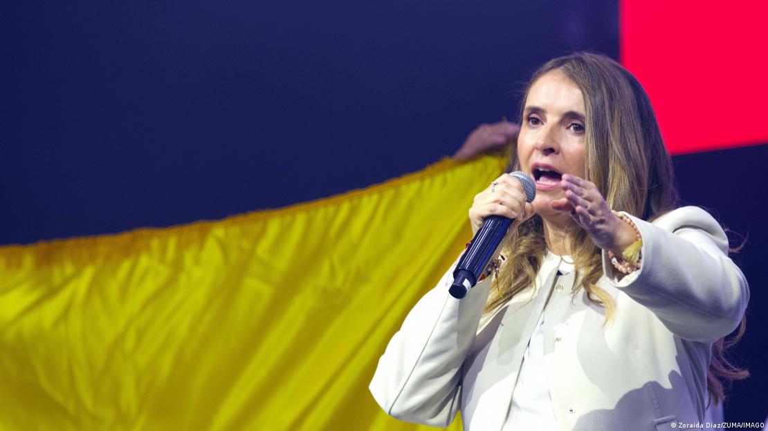 Paloma Valencia fala ao microfone em frente a uma bandeira da Colômbia Paloma Valencia fala ao microfone em frente a uma bandeira da Colômbia