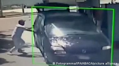 Image 7: A CCTV image taken at a petrol station shows a man holding a car door closed. The car is on fire.