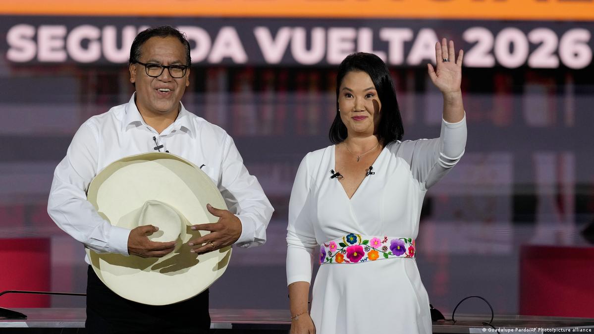 Presidential candidate Keiko Fujimori waves prior to a televised debate with her rival Roberto Sanchez. He is carrying a large cowboy hat, she is dressed in a white dress with a floral belt.