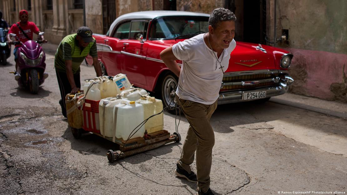Personas transportan agua en envases plasticos junto a un oldtimer rojo. Personas transportan agua en envases plasticos junto a un oldtimer rojo.
