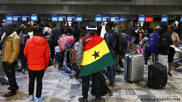 A man draped in a Ghana flag stands among other Ghanaians as Ghana repatriates hundreds of its citizens from South Africa on May 27, 2026