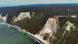 Aerial view of the white chalk cliffs in Jasmund National Park on the island of Rügen, showing a steep coastline, dark Baltic Sea waters, and forested cliffs. On the right side, the modern Königsstuhl skywalk extends over the chalk cliffs. Aerial view of the white chalk cliffs in Jasmund National Park on the island of Rügen, showing a steep coastline, dark Baltic Sea waters, and forested cliffs. On the right side, the modern Königsstuhl skywalk extends over the chalk cliffs.