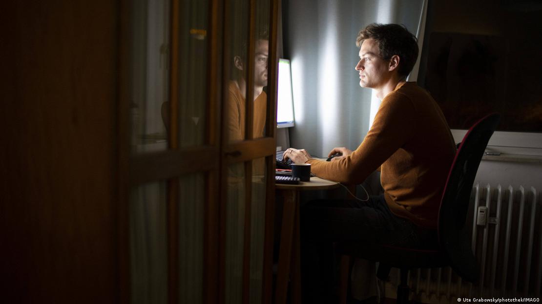 Homem sentado junto a uma escrivaninha em frente a computador 