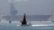 A small submarine in the foreground, a large aircraft carrier in the background