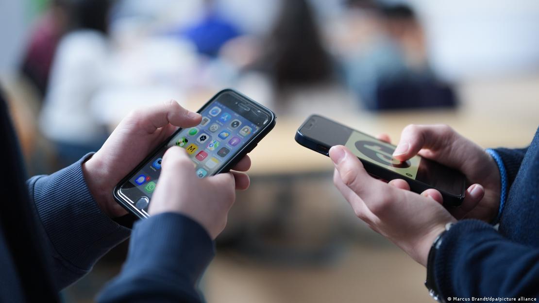 Bir sınıfta yan yana duran iki öğrenci, ellerindeki akıllı telefonları kullanıyor.