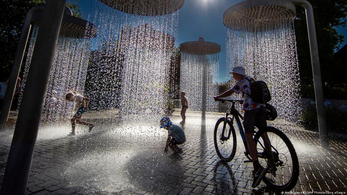 Children cool off in a public fountain in Vilnius, Lithuania, one on a bike