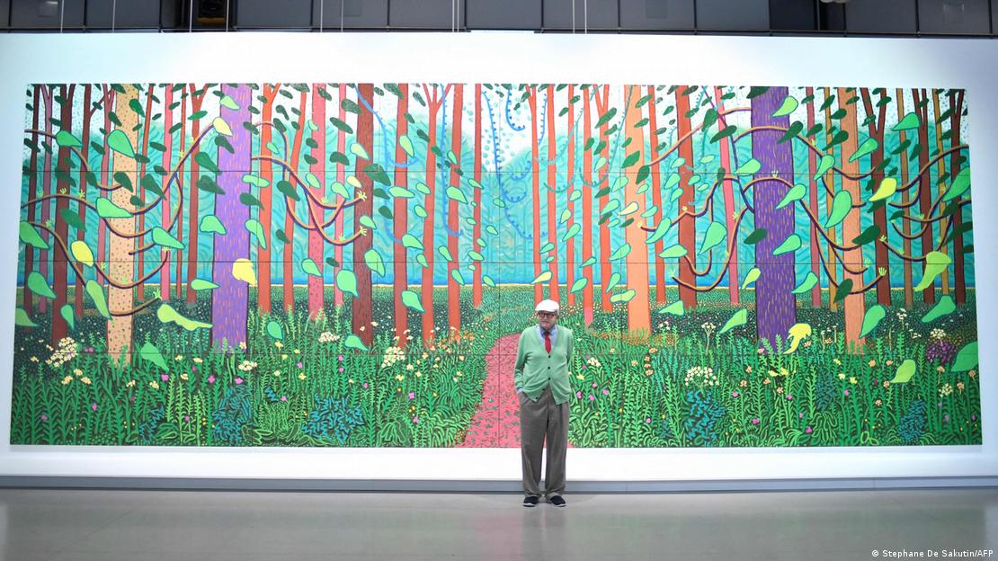 David Hockney posa ante un gran mural hecho por él. David Hockney posa ante un gran mural hecho por él.
