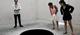 Three people look at a black circle on the floor 'Descent into Limbo' by Anish Kapoor.