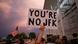 Un hombre sostiene un cartel con la leyenda "Tú no eres JFK", en señal de protesta mientras la gente observa las obras para retirar el nombre de Donald Trump de la señalización del Centro Kennedy. (12.06.2026)