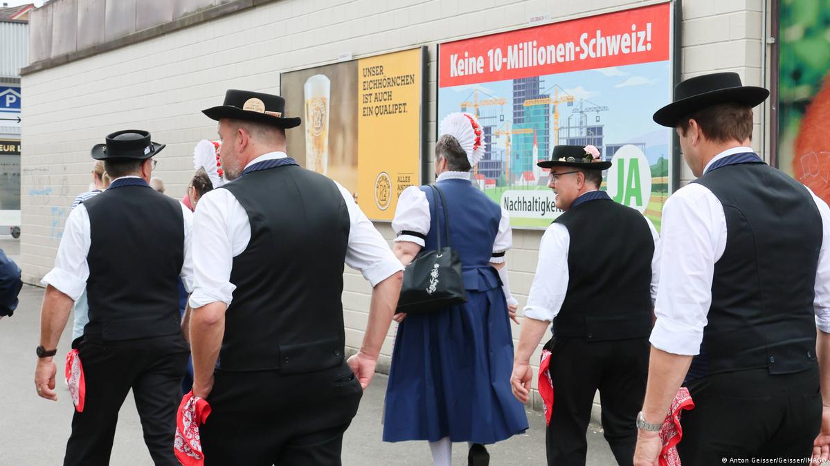 People in Swiss national costume in front of a poster saying 'No 10-million Switzerland'