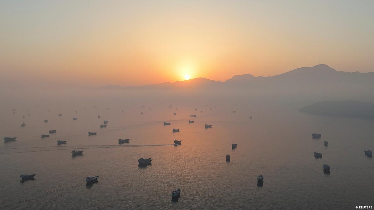Vessels in the Strait of Hormuz with the sun partially visible from behind a distant mountain in Oman, June 15, 2026.