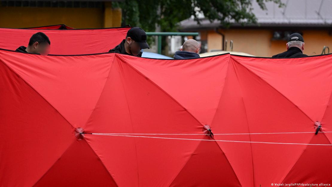 La policía revisa el lugar del crimen tras unos biombos rojos.