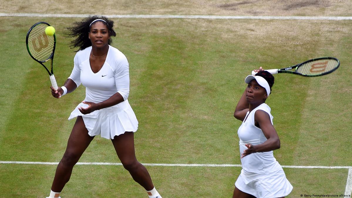 Serena and Venus Williams both hold up their racquets to strike during a doubles match