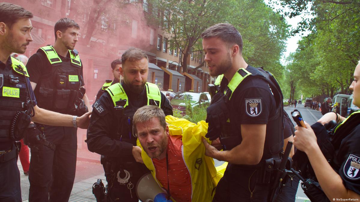 Police carrying away a demonstrator in a yellow suit in front of the SuperReturn meeting in Berlin in June