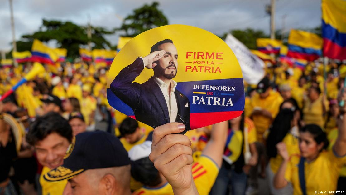 Mão segura leque com foto do candidato Abelardo de la Espriella batendo continência frente a multidão de pessoas com camisa amarela