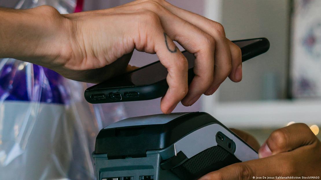 Yakın çekimde elinde akıllı telefon tutan bir kişi, alışveriş sonrası kasada telefonu POS cihazına tutarak dijital ödeme yapıyor