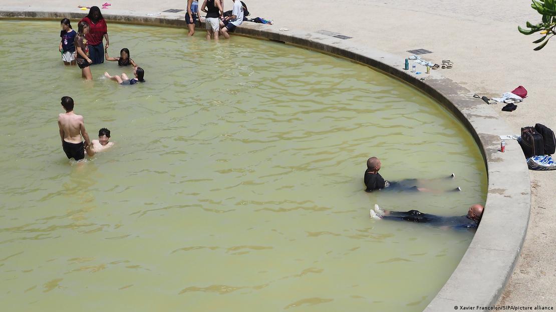 Crianças e moradores de rua se banham dentro de fonte pública com água turva em um parque de Paris durante a onda de calor extremo