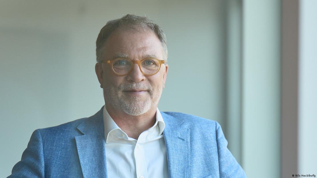 Ein Mann mit Brille, hellblauem Jackett und weißem Hemd schaut freundlich in die Kamera Ein Mann mit Brille, hellblauem Jackett und weißem Hemd schaut freundlich in die Kamera