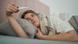 Una mujer echada en una cama mira el termómetro que tiene en la mano. Una mujer echada en una cama mira el termómetro que tiene en la mano.