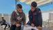 University students attend classes at an outdoor table under a shade. Two young men are looking at a textbook together. University students attend classes at an outdoor table under a shade. Two young men are looking at a textbook together.