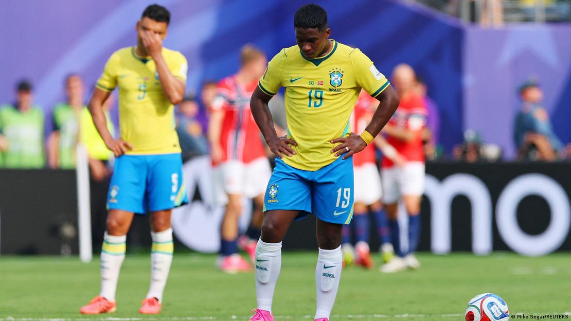 Hendrick com as mãos na cintura, olha para baixo, com outro jogador brasileiro com a mão nos olhos ao fundo Hendrick com as mãos na cintura, olha para baixo, com outro jogador brasileiro com a mão nos olhos ao fundo