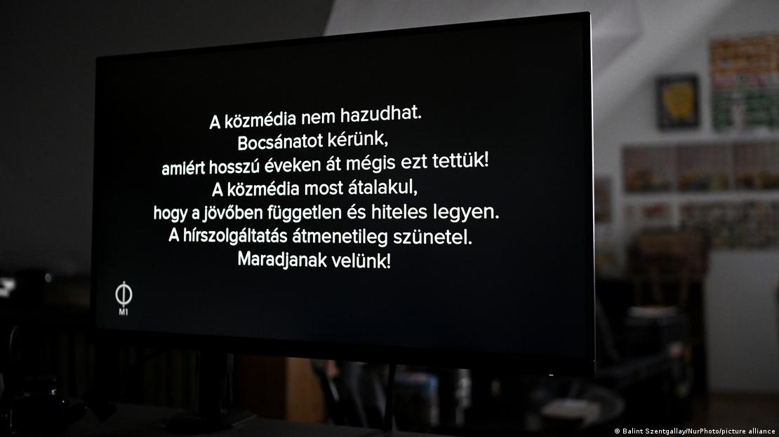 Bir odanın içindeki ekranda, siyah fon üzerine beyaz harflerle Macarca bir yazı