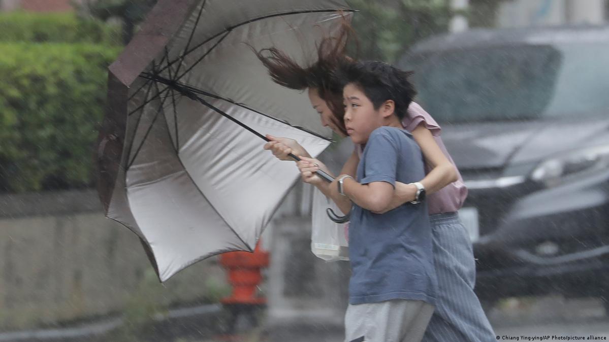 图为一名女子及孩童在台风中撑伞行走