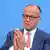 Das Bild zeigt einen älteren Mann im blauen Anzug, Bundeskanzler Friedrich Merz, vor der Bundespressekonferenz in Berlin, er hat die Hände vor seinen Brust gefaltet