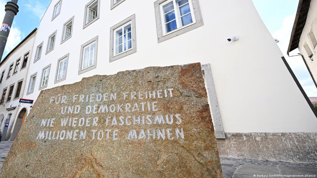 Fotoğrafta Braunau am Inn'deki binanın cephesi ve ön planda anıt taşı yer alıyor. Taşın üzerinde "Barış, özgürlük ve demokrasi için. Bir daha asla faşizm. Milyonlarca ölü uyarıyor" yazıyor Fotoğrafta Braunau am Inn'deki binanın cephesi ve ön planda anıt taşı yer alıyor. Taşın üzerinde "Barış, özgürlük ve demokrasi için. Bir daha asla faşizm. Milyonlarca ölü uyarıyor" yazıyor