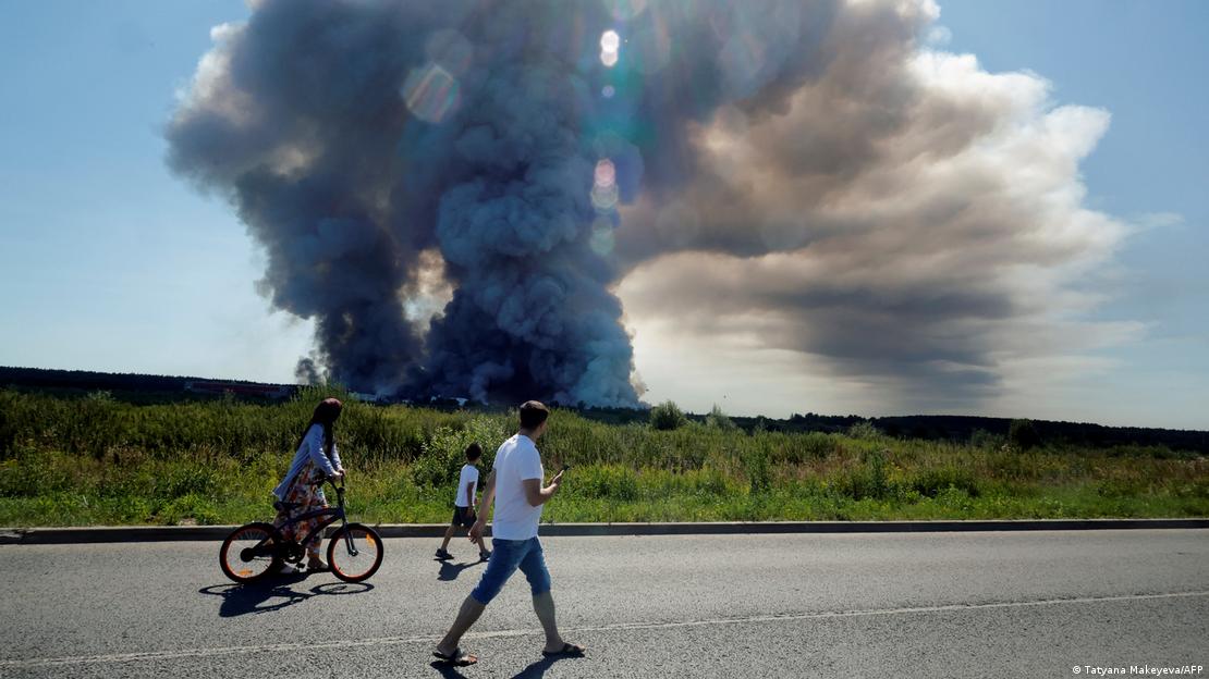 Personas a pie y en bicicleta pasan por el lugar donde Ucrania atacó con drones, mirando una columna de humo en el horizonte. Personas a pie y en bicicleta pasan por el lugar donde Ucrania atacó con drones, mirando una columna de humo en el horizonte.