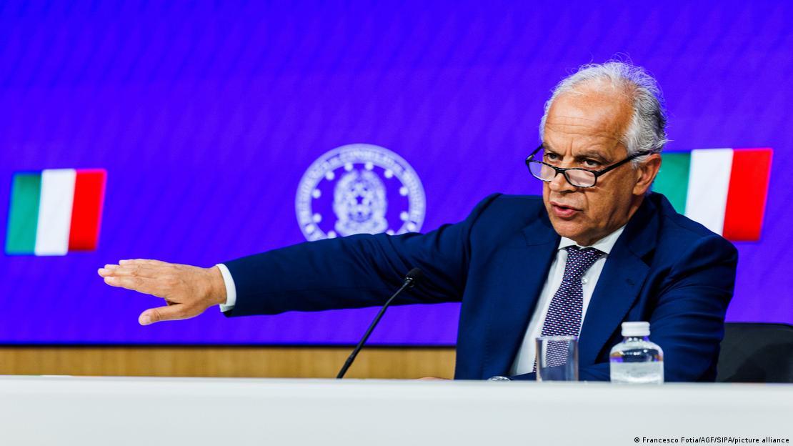 İtalya İçişleri Bakanı Matteo Piantedosi, sağ kolu göğüs hizasında havaya kalkmış halde konuşma yapıyor, arka plandaki dev ekranda iki İtalya bayrağı ve bir logo
