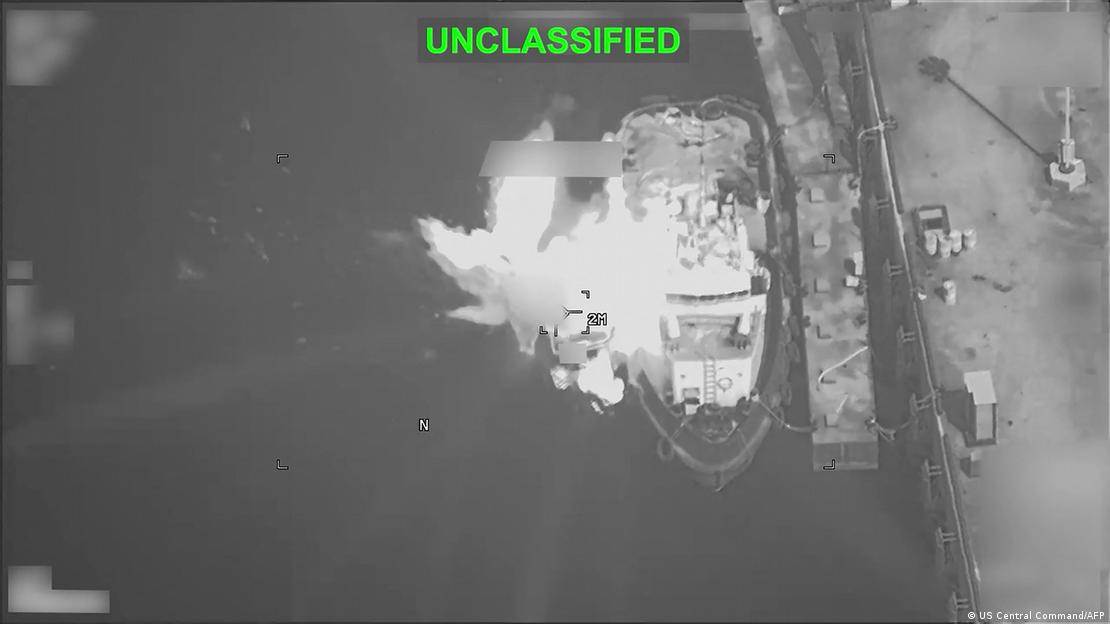 Grainy black-and-white aerial photo of an explosion on a ship beside a dock. The image has UNCLASSIFIED written in green across the top. Grainy black-and-white aerial photo of an explosion on a ship beside a dock. The image has UNCLASSIFIED written in green across the top.