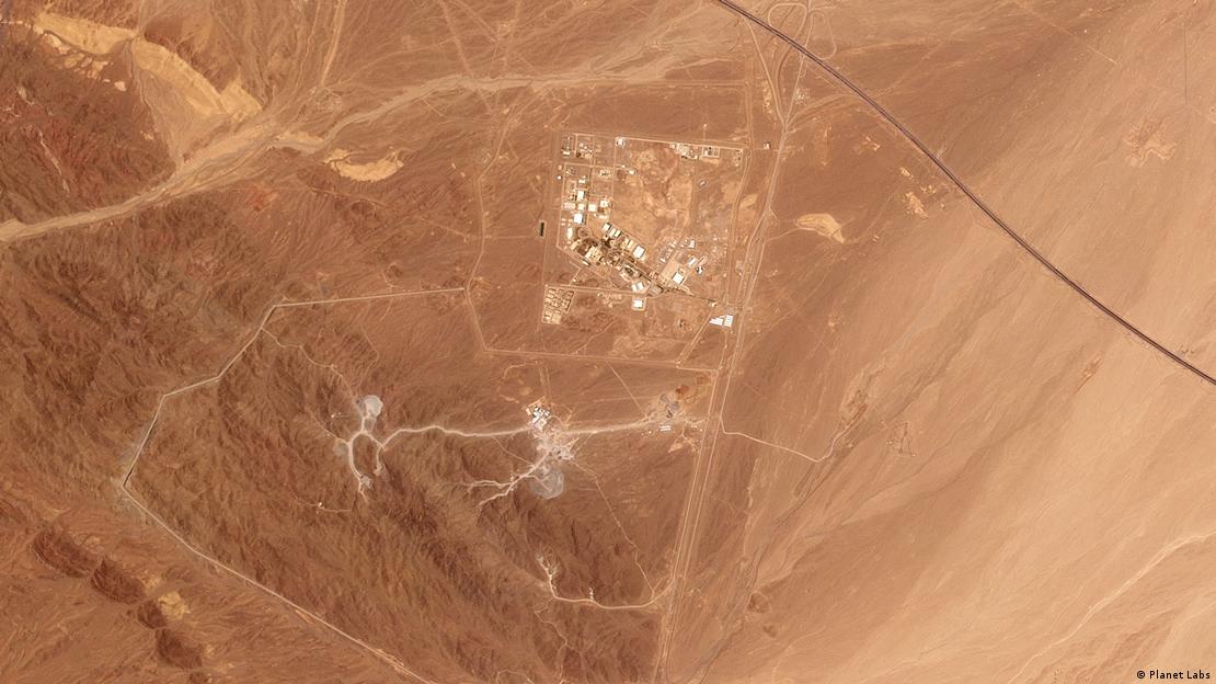 A muted-orange satellite photo showing some white dots of buildings surrounded by deserted rocky mountains and a few small roads. A muted-orange satellite photo showing some white dots of buildings surrounded by deserted rocky mountains and a few small roads.