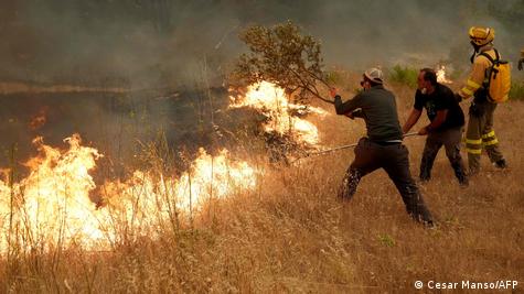 Tres personas, de las que sólo uno lleva uniforme de los servicios de emergencias, tratan de extinguir las llamas que avanzan por los matojos secos.