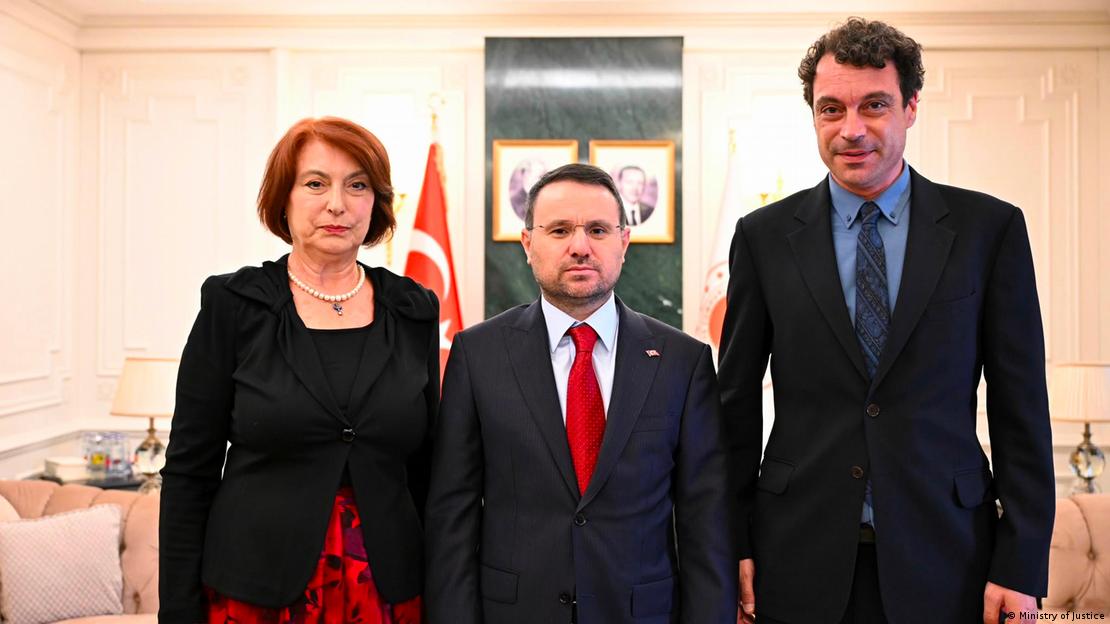 Üç kişi, resmi bir makam odasında yan yana kameraya poz verirken arkalarında Türk bayrağı ve duvarda çerçeveli fotoğraflar görülüyor Üç kişi, resmi bir makam odasında yan yana kameraya poz verirken arkalarında Türk bayrağı ve duvarda çerçeveli fotoğraflar görülüyor