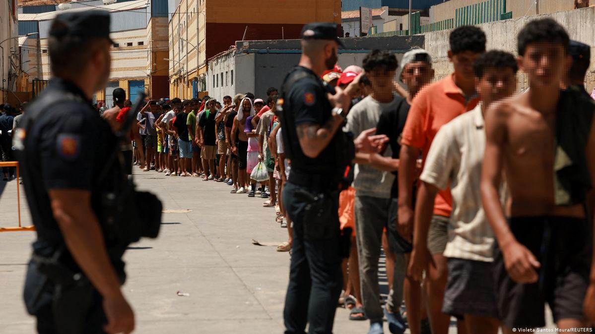 Migrants queue to receive food staples from local NGO Media Luna Blanca in an industrial area where they are sleeping amid recent mass crossings by migrants on foot and by sea from Morocco into the Sp
